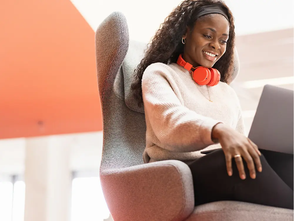 Een Henkel werknemer zit in een comfortabele zetel met haar laptop op haar knieën. Ze lacht.