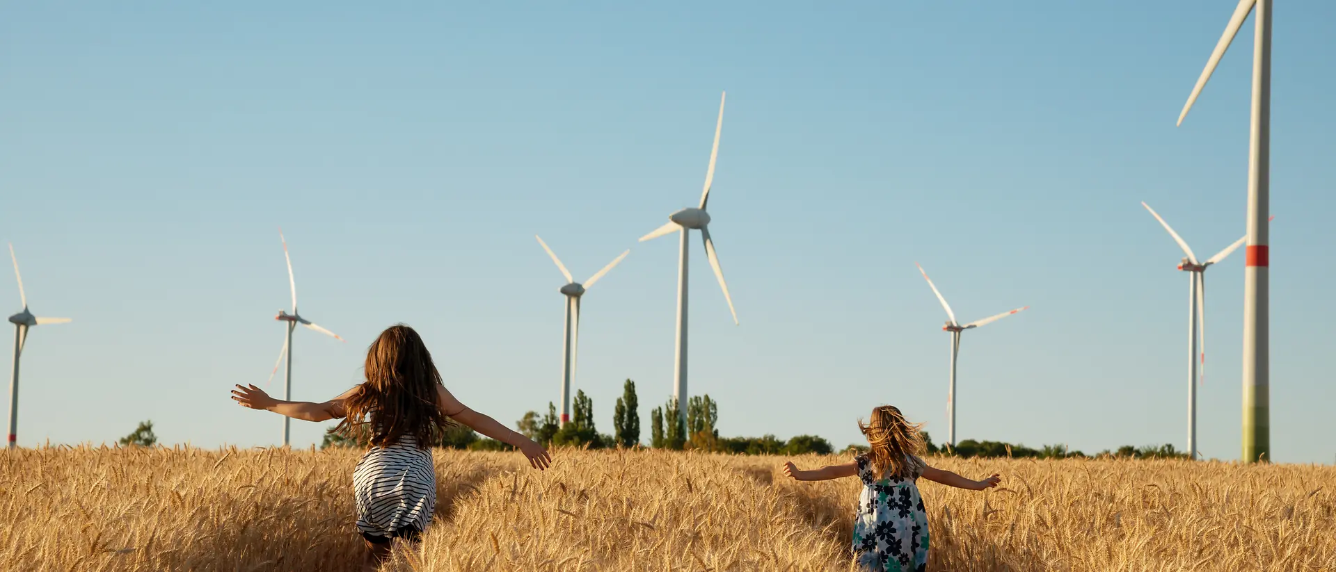 2 meisjes rennen in een maïsveld met moderne windmolens op de achtergrond