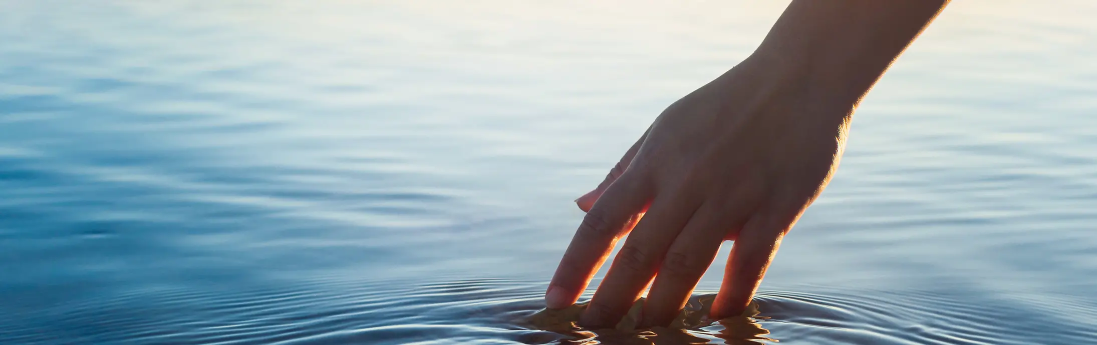 Een hand strijkt door een kalm wateroppervlak voor de horizon