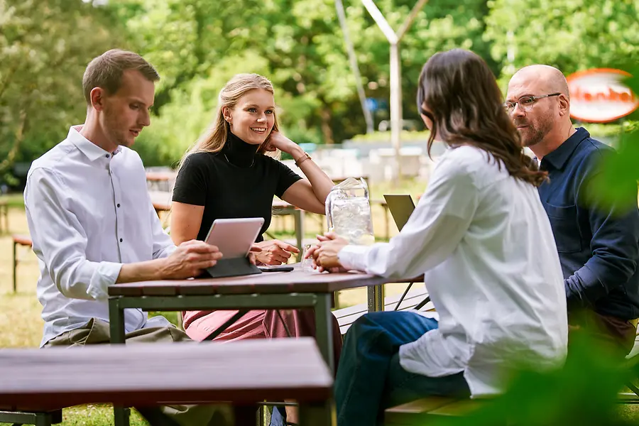 Groep collega's die buiten samenzitten en werk bespreken met tablets en laptops, als illustratie van samenwerking en een open, teamgerichte cultuur bij Henkel.
