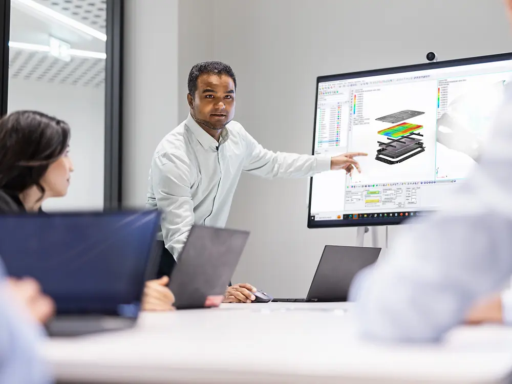 Team werkt samen aan innovatie met Loctite-oplossingen, terwijl een professional modellerings- en simulatieontwerpen presenteert op een groot scherm tijdens een technische vergadering.