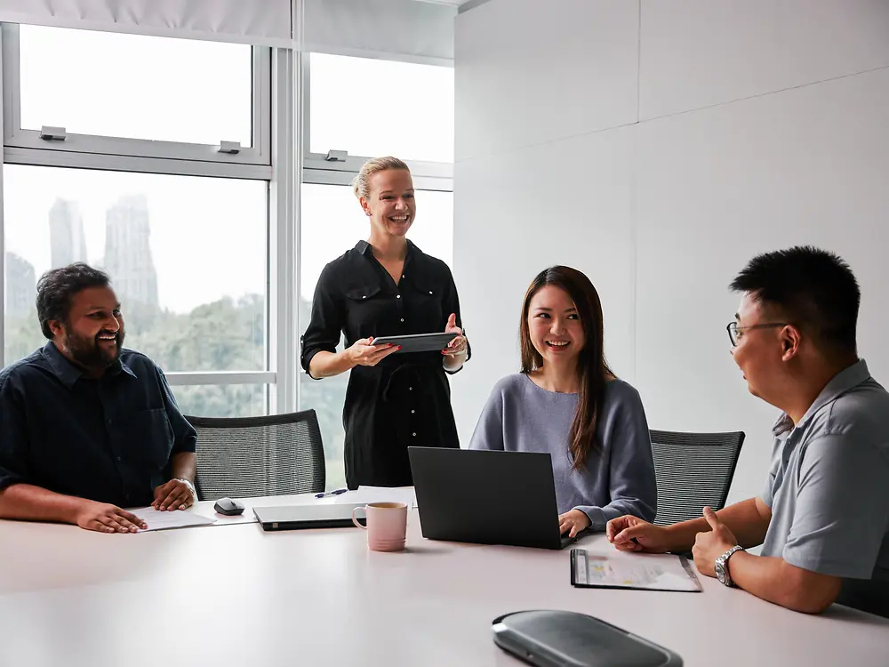 Een diverse groep professionals in een moderne vergaderzaal, die samenwerken rond een tafel met laptops en documenten. De scène weerspiegelt Henkels engagement voor genderpariteit en diversiteit in leiderschap, en toont een inclusieve werkomgeving waarin verschillende perspectieven bijdragen aan de besluitvorming.