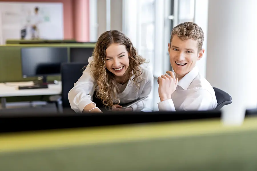 Twee jonge professionals werken samen aan een bureau in een moderne kantooromgeving, ter illustratie van studentenjobs en instapfuncties.