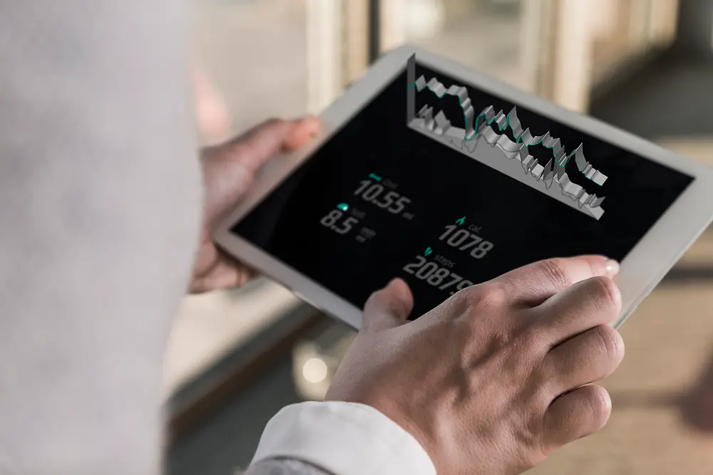 Een persoon in een licht interieur met een tablet in de hand waarop van over zijn schouder digitale grafieken en cijfermateriaal te zien zijn.